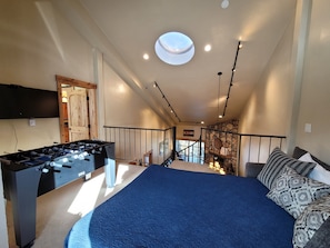A room with a foosball table, a bed with patterned pillows, a staircase, and a skylight.