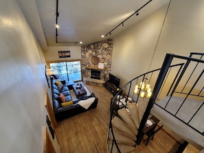 A modern living room with a stone fireplace, a black leather sofa, and a wooden staircase.