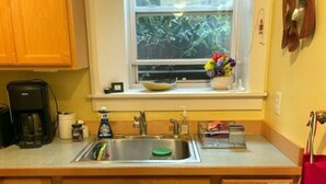 Une cuisine avec des meubles en bois, un évier, une machine à café et une fenêtre donnant sur un paysage verdoyant.