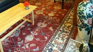 Un salon avec un canapé foncé, un fauteuil rouge, une table basse en bois sur laquelle se trouve un vase, un grand vase décoratif et un téléviseur.