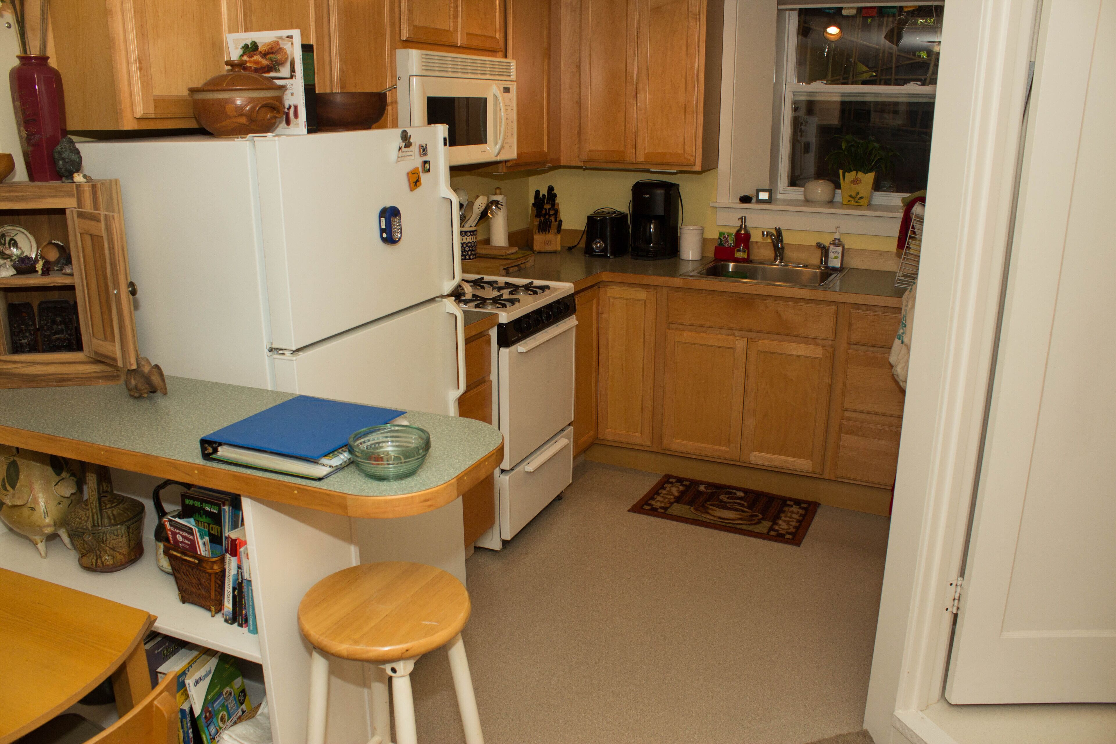 Une cuisine de taille réduite, dotée de meubles en bois, d’un réfrigérateur blanc, d’un four à micro-ondes, d’une cuisinière et d’un évier.