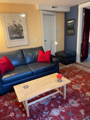 A living room with a blue leather sofa, a wooden coffee table, and a red rug.