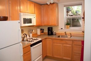 Compact kitchen with a sink, stove, refrigerator, and dishwasher, offering a view of the outside through the window above the sink.