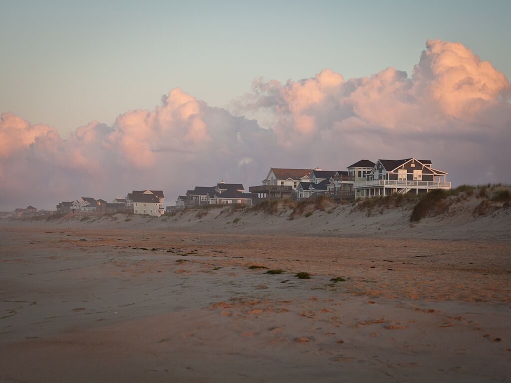 Een strandpand met meerdere huizen, waaronder een groot huis met balkon en een kleiner huis op de achtergrond.