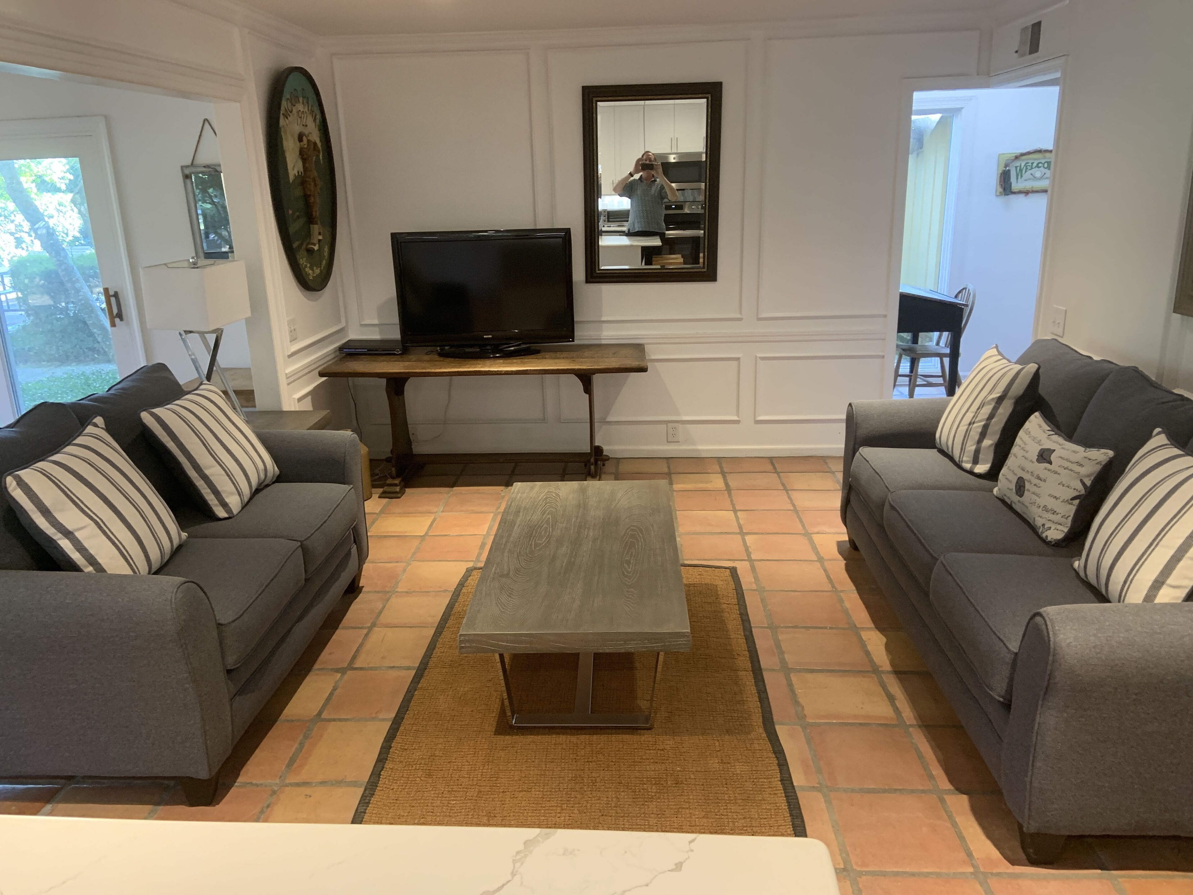 Una sala de estar con dos sofás grises, una mesa de centro, un televisor sobre un mueble de madera y un piso de baldosas.