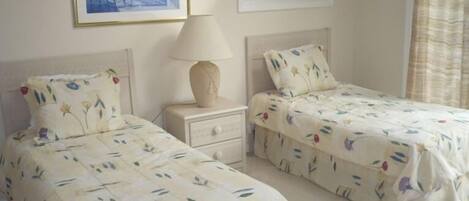 Un dormitorio con dos camas individuales, una mesita de noche con lámpara y un cuadro enmarcado en la pared.