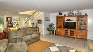 Ein geräumiges Wohnzimmer mit einer großen Eckcouch, einem TV-Schrank mit Regalen und einer Treppe, die in ein Obergeschoss führt.