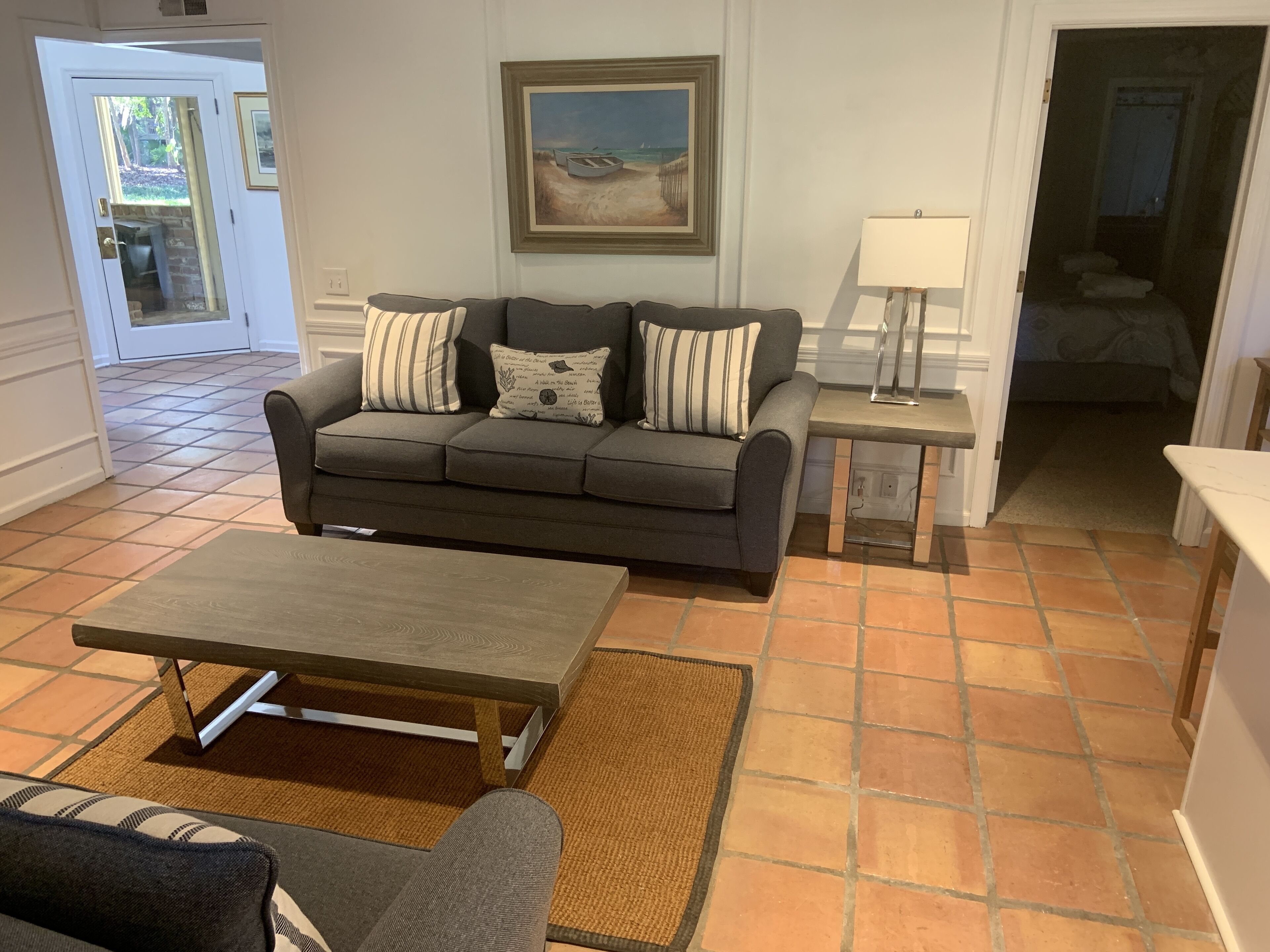 Uma sala de estar com sofá, mesa de centro, quadro e abajur.