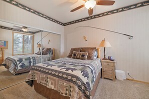 Une chambre avec deux lits, un ventilateur de plafond, une table de chevet avec une lampe et une horloge fixée au mur.