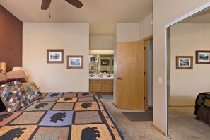 A bedroom with a bed, a bedside table, a lamp, and a quilt. There is a door leading to a bathroom with a mirror and a sink.