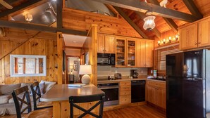A wooden cabin interior with a kitchen, dining area, and a living space. - Heather Heights Cottage - Cozy cabin with a View and Fire Pit, minutes to Boone! (Boone)