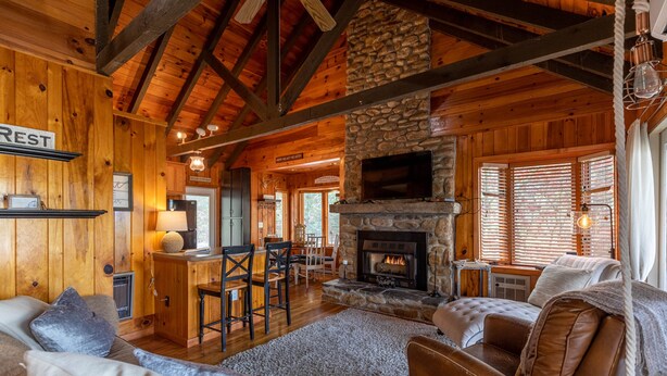 A rustic cabin interior with a stone fireplace, wooden walls, and a cozy seating area. - Heather Heights Cottage - Cozy cabin with a View and Fire Pit, minutes to Boone! (Boone)