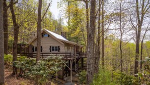 A cabin with a wooden deck and a staircase leading up to it, surrounded by trees and greenery. - Heather Heights Cottage - Cozy cabin with a View and Fire Pit, minutes to Boone! (Boone)