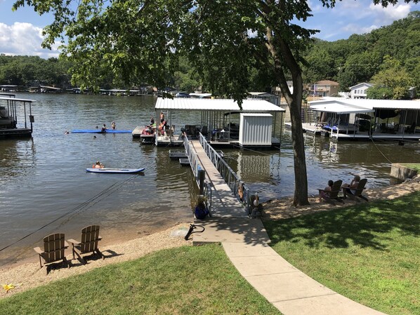 A lakeside dock with boats, a covered seating area, and a grassy area with chairs.