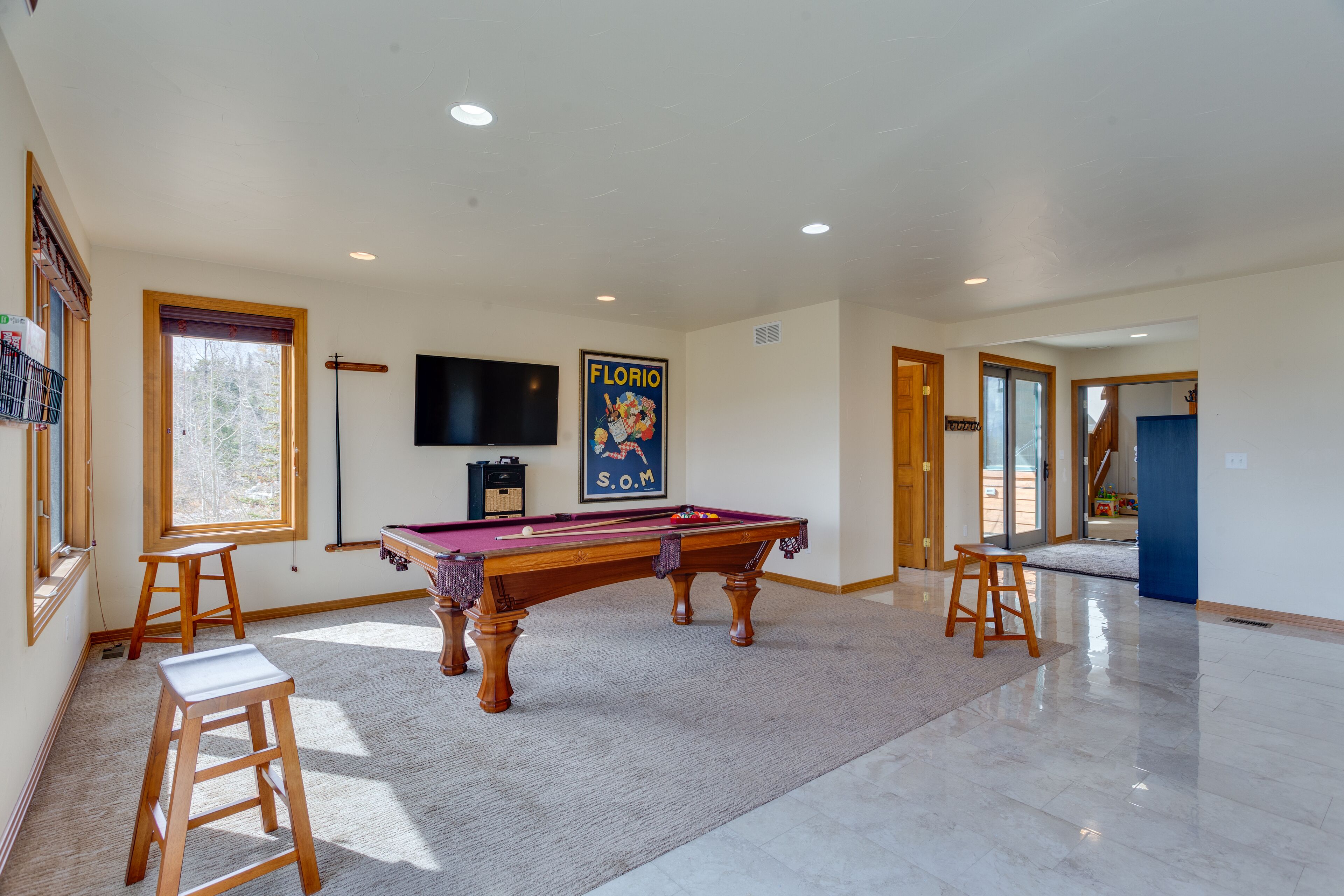 Une pièce spacieuse équipée d’une table de billard, de tabourets en bois, d’un téléviseur fixé au mur et d’une affiche accrochée au mur.