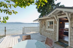 A wooden deck with a glass table and chairs overlooking a lake.