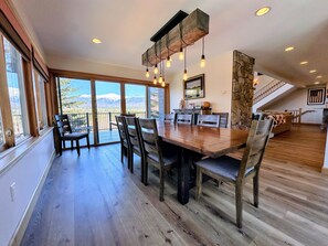 A spacious dining area with a large wooden table and chairs, a stone accent wall, and a view of mountains through large windows.