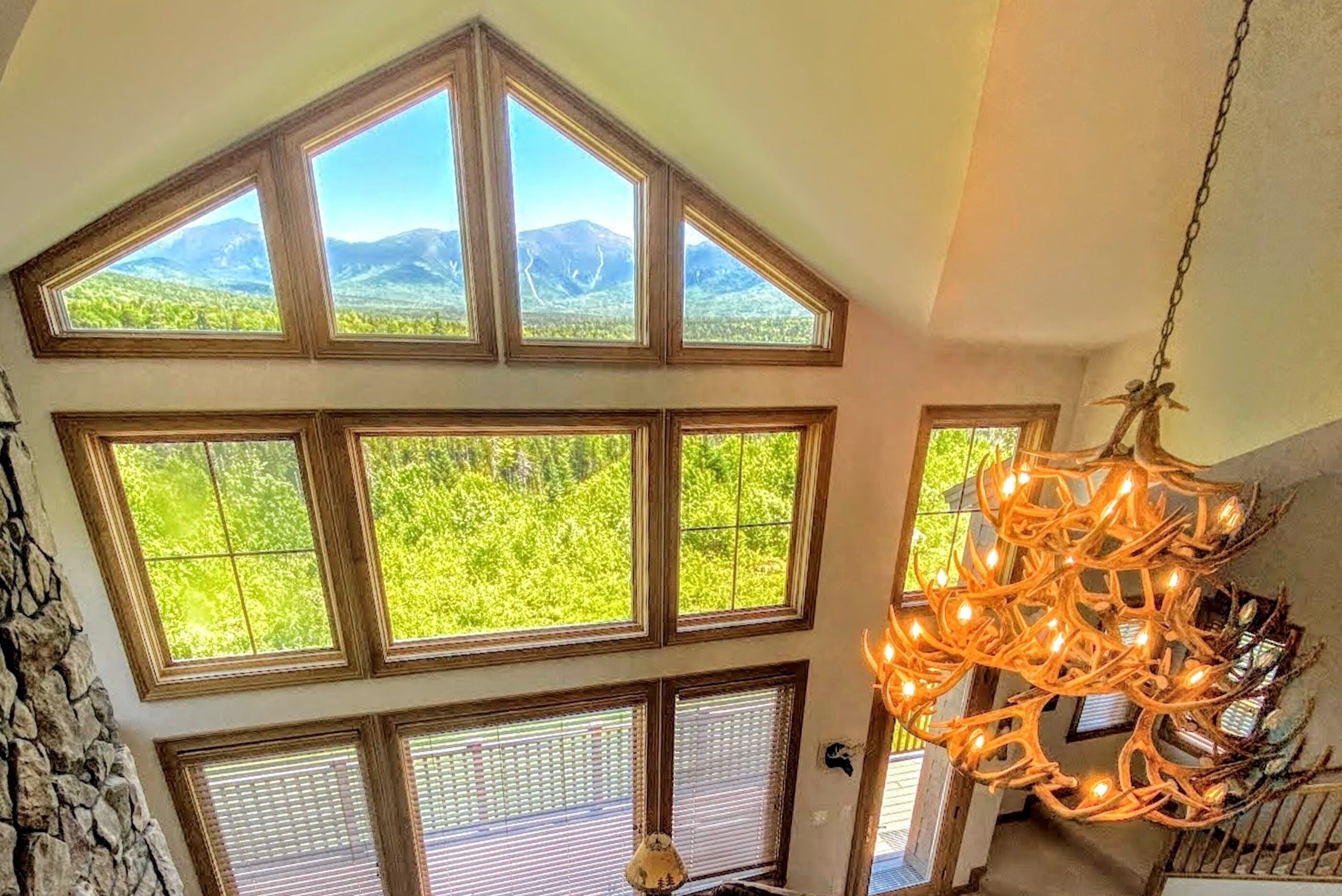 Habitación con ventanas amplias que ofrecen vistas a montañas y vegetación. Destaca una lámpara de araña con adornos similares a astas.
