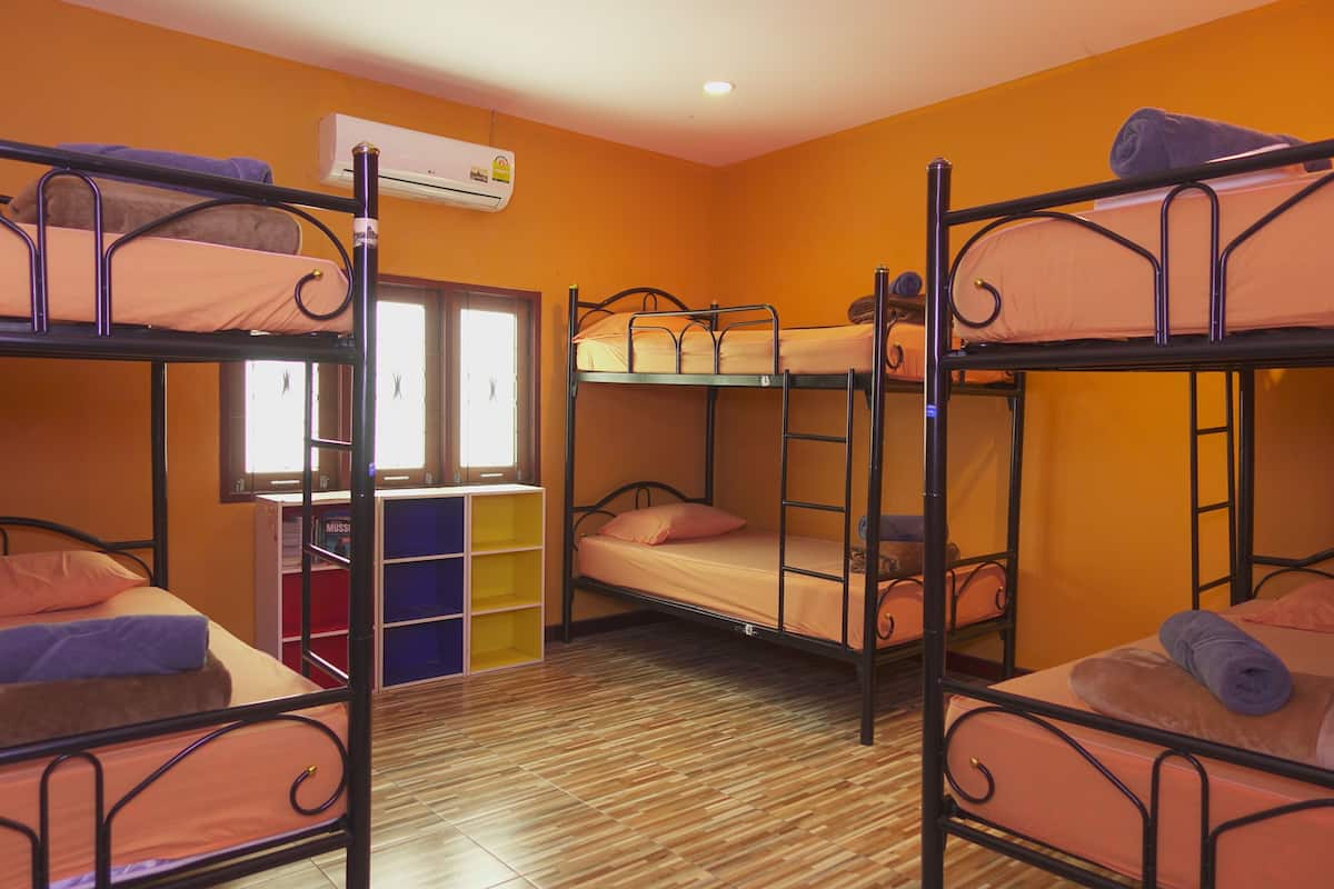 A dormitory room with bunk beds, an air conditioning unit, a window, and a bookshelf.
