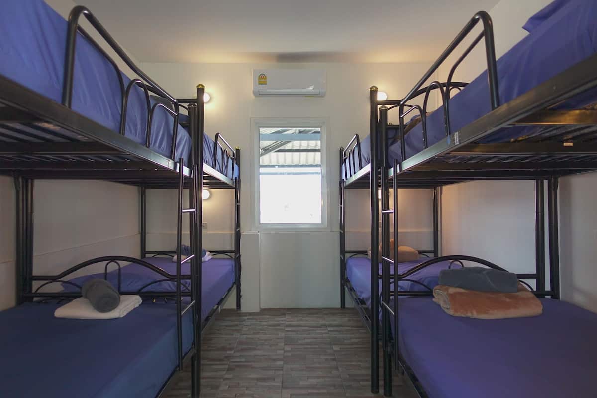 A dormitory room with bunk beds, a window, and an air conditioning unit.