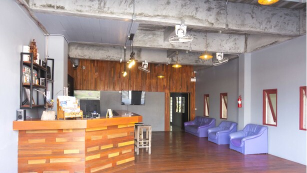 A reception area with a wooden counter, a seating area with purple chairs, and a wooden wall with a mounted television. - Blessing Backpackers (Ko Pha-ngan)
