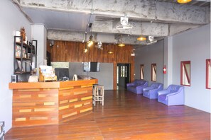 A reception area with a wooden counter, a seating area with purple chairs, and a wooden wall with a mounted television. - Blessing Backpackers (Ko Pha-ngan)