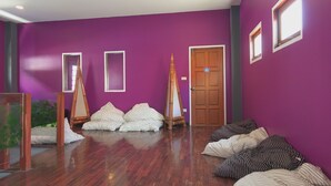 A room with purple walls, wooden flooring, and a door with a blue sign. There are several pillows and a small easel. - Blessing Backpackers (Ko Pha-ngan)