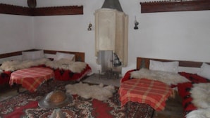 A traditional room with two beds, a central heating stove, and a patterned rug. - Rooms Merlika (Krujë)