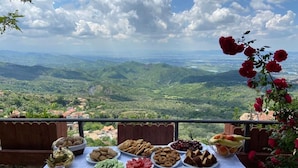 A table with various food items and a scenic view of mountains and valleys. - Rooms Merlika (Krujë)
