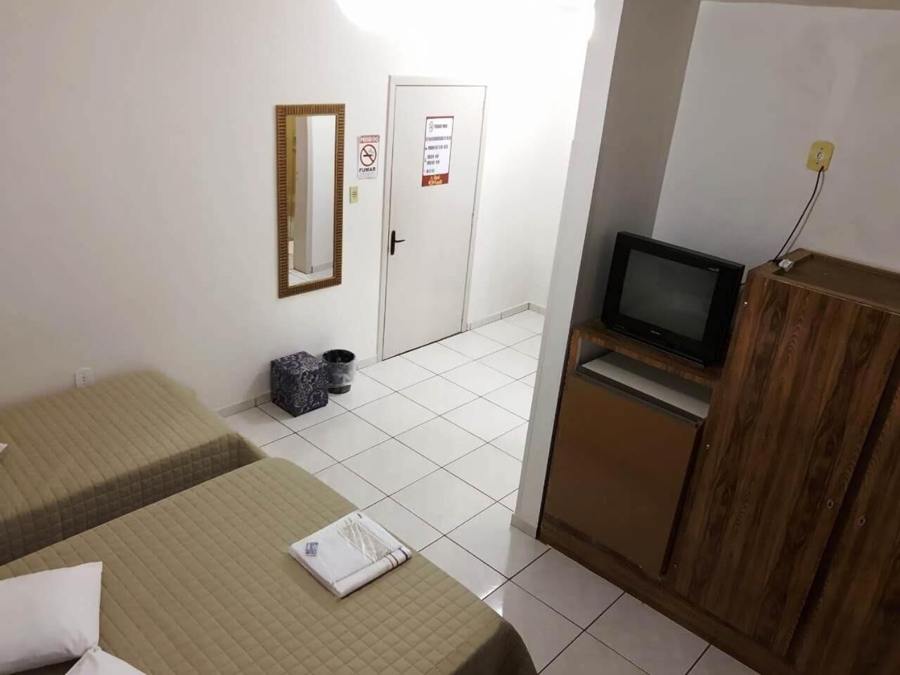 Une petite chambre d’hôtel avec deux lits simples, une télévision, une armoire et une porte sur laquelle est apposée une pancarte « Il est interdit de fumer ».