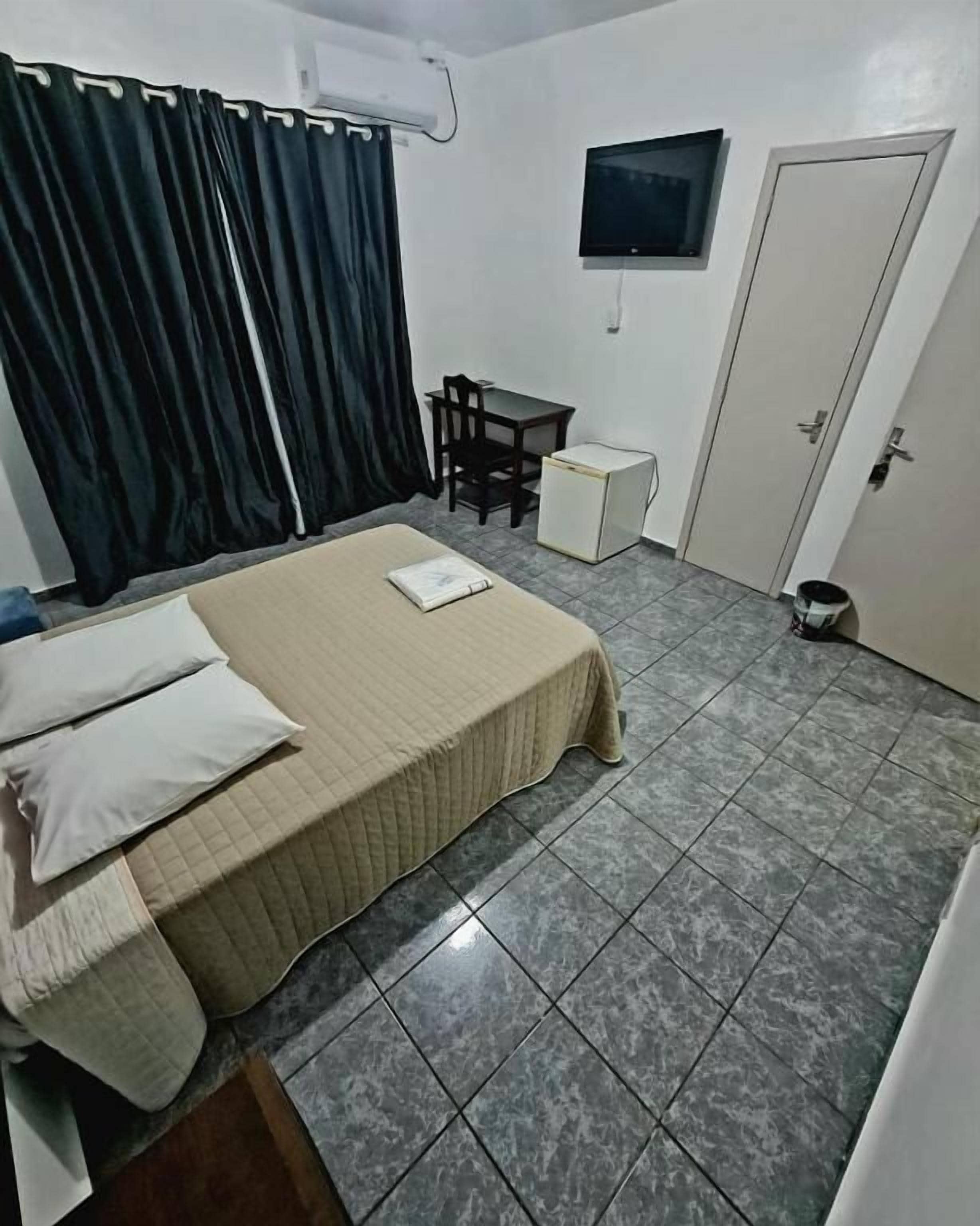 Un dormitorio con cama, escritorio, silla, televisor y puerta.