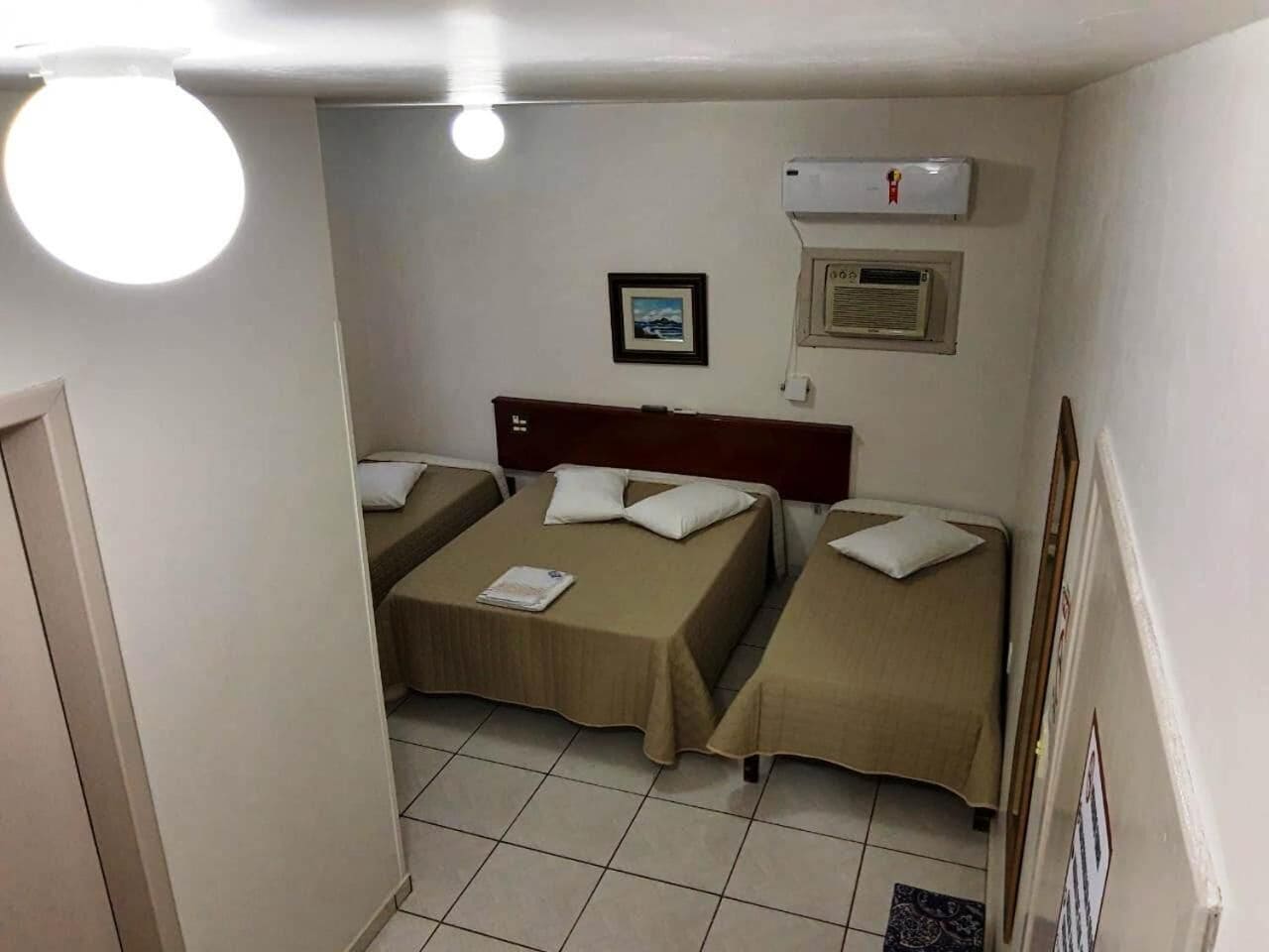 A small, clean room with two single beds, a headboard, an air conditioning unit, and a framed picture on the wall.