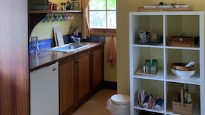 A kitchen with wooden cabinets, a sink, a microwave, and a window with curtains. There is a shelf with kitchenware and a trash bin. - Relax in a beautiful private peaceful setting 5 minute drive from Beechworth (Wooragee)