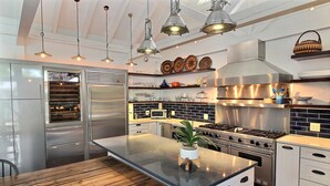 A modern kitchen with stainless steel appliances, a central island, hanging pendant lights, and decorative plates on the wall. - Blu on White- 4BR Old Town Key West Home with Heated Pool (Key West)