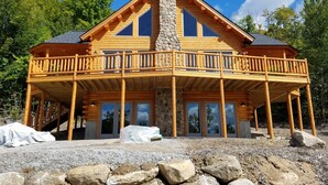 Una baita di legno con camino in pietra, balcone in legno e diverse finestre.