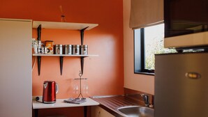 Eine Küche mit roter Wand, einem weißen Regal mit Küchenutensilien, einem Wasserkocher und einem Fenster.