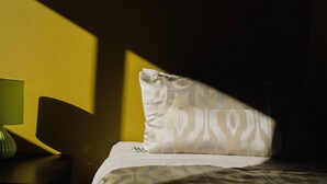 Ein ordentlich bezogenes Bett mit einem gemusterten Kopfkissen und einer grünen Lampe auf einem Nachttisch.