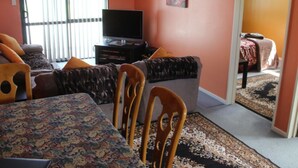 Ein Wohnzimmer mit einer Couch, Sesseln, einem Fernseher und einer gemusterten Tischdecke.
