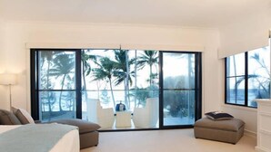 A bedroom with a large sliding glass door leading to a balcony, a bed, a small seating area, and a nightstand.