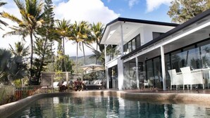 A modern pool area with clear water, surrounded by palm trees and a contemporary building with large windows and outdoor seating.