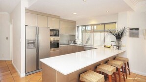 Een moderne keuken met een groot eiland, roestvrijstalen apparatuur en uitzicht naar buiten.