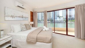Een slaapkamer met een groot bed, een nachtkastje, een spiegel en een uitzicht op een stadslandschap door grote ramen.