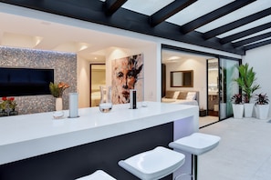 A modern interior with a white reception desk, bar stools, a large abstract painting, and a tiled wall.