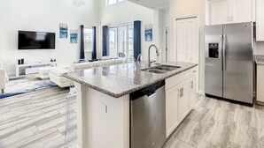 A modern kitchen with a central island, stainless steel appliances, and a flat-screen TV mounted on the wall.