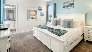 A bedroom with a white bed, a nightstand, a dresser, a mirror, and a painting on the wall.