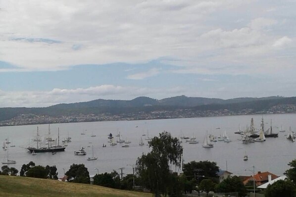 Ein Hafen mit mehreren Segelbooten und Yachten, umgeben von Hügeln und einer in der Ferne liegenden Stadtlandschaft.