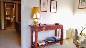 Ein Holzkonsolentisch mit Lampe, Büchern und gerahmten Pflanzenmotiven an der Wand.