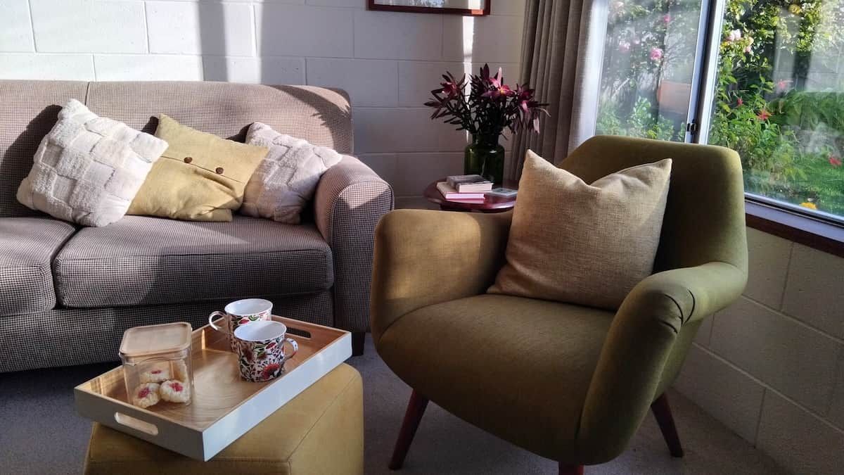 A living room with a sofa, armchair, and a window with a view of greenery.