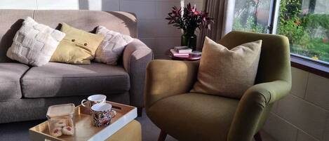 A living room with a sofa, armchair, and a window with a view of greenery.