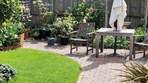 A patio area with a wooden table and chairs, surrounded by potted plants and a small lawn. - Peaceful Garden Retreat in Sandy Bay. (Sandy Bay)